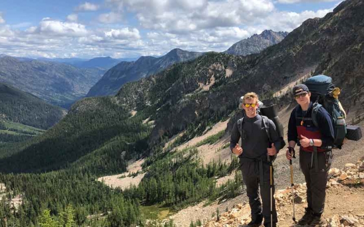 two students pause for a photo in front of a mountain landscape while hiking in the pacific northwest
